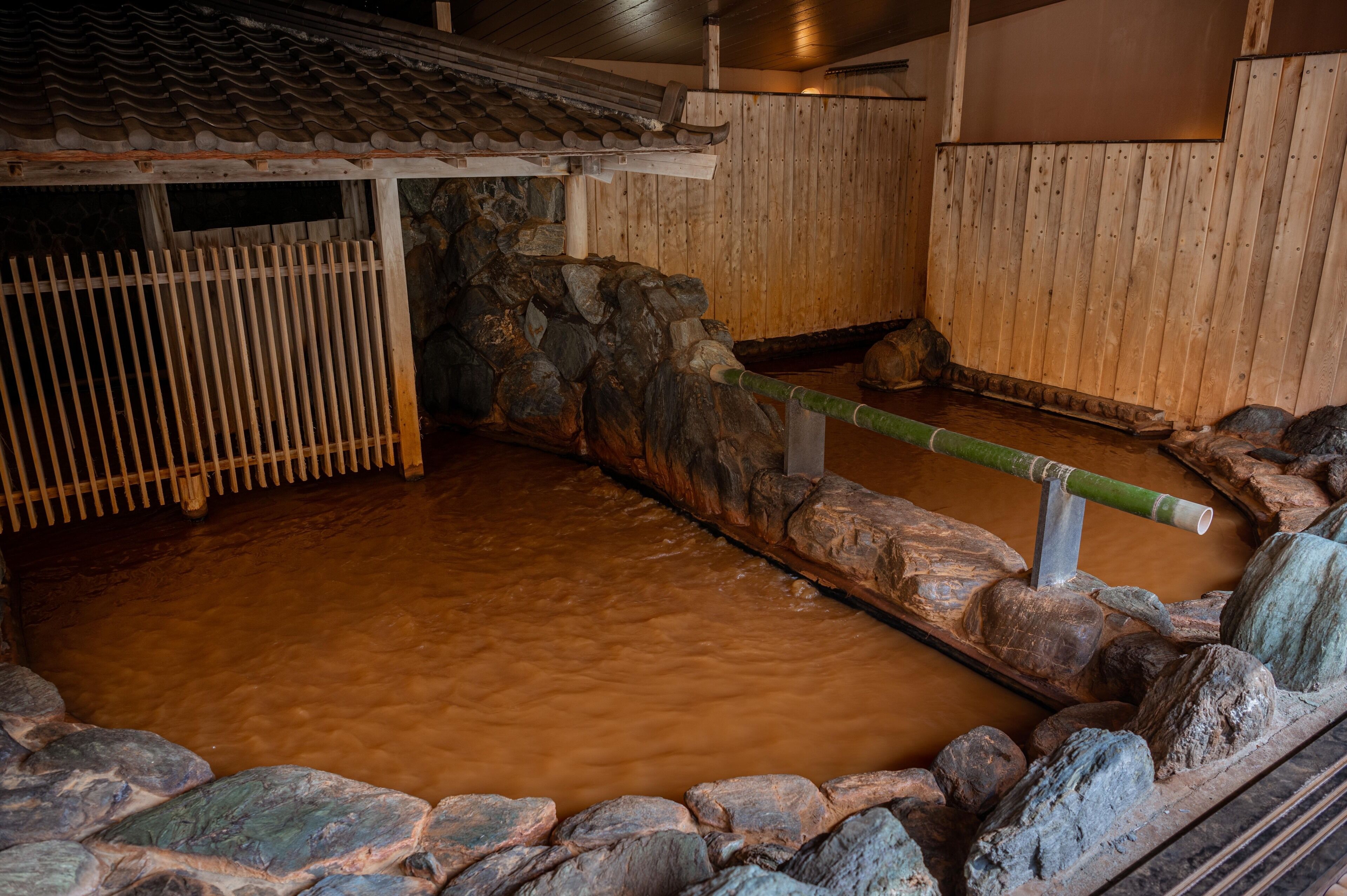 A traditional Japanese onsen with a stone bath, wooden walls, and a tiled roof.