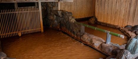 A traditional Japanese onsen with a stone bath, wooden walls, and a tiled roof.