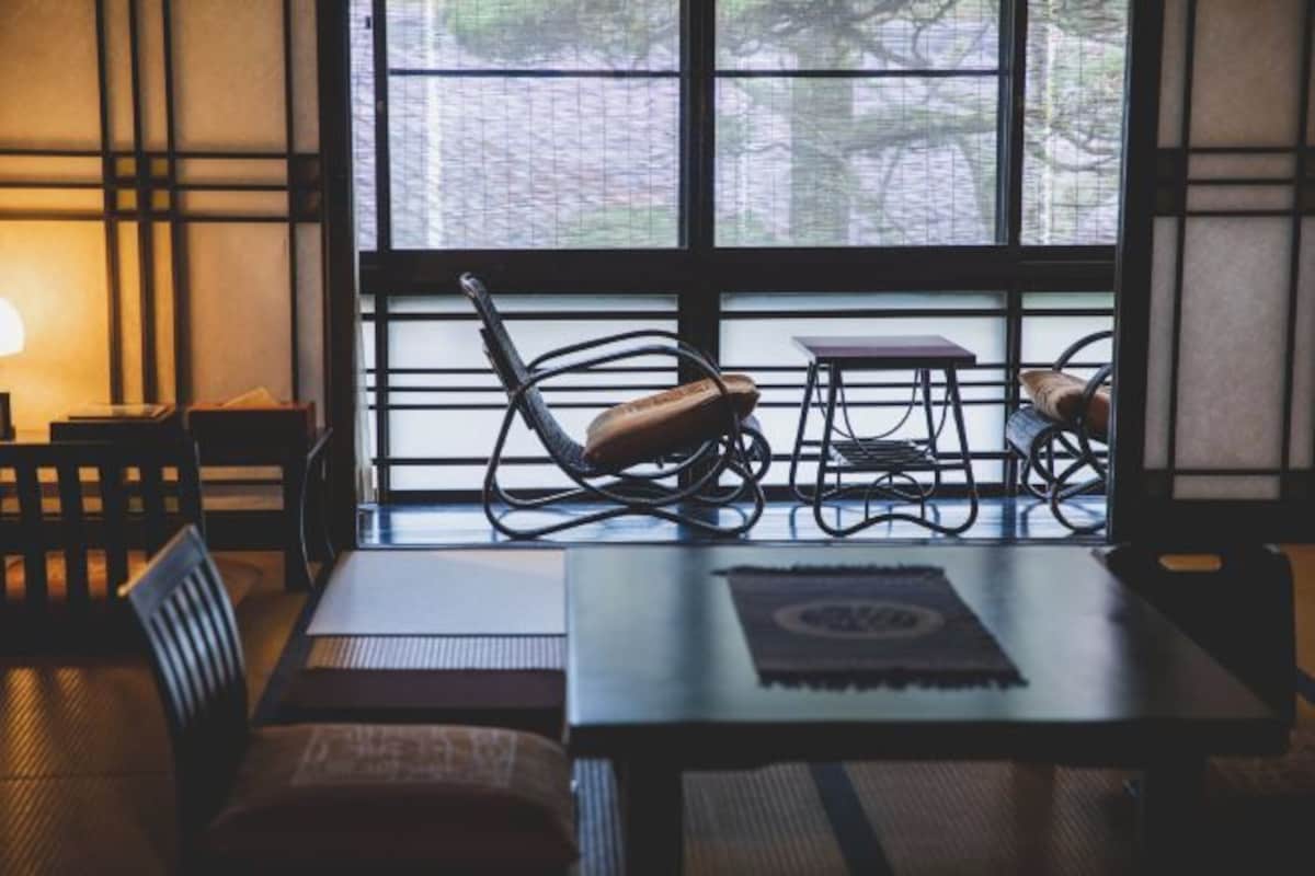 Una habitación con decoración tradicional japonesa, que incluye esteras de tatami, una mesa baja con posavasos y vistas amplias a través de grandes ventanales.