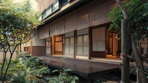 A traditional Japanese-style building with tatami mat flooring, a wooden deck, and a garden with rocks and plants. - Tocen Goshoboh (Kobe)
