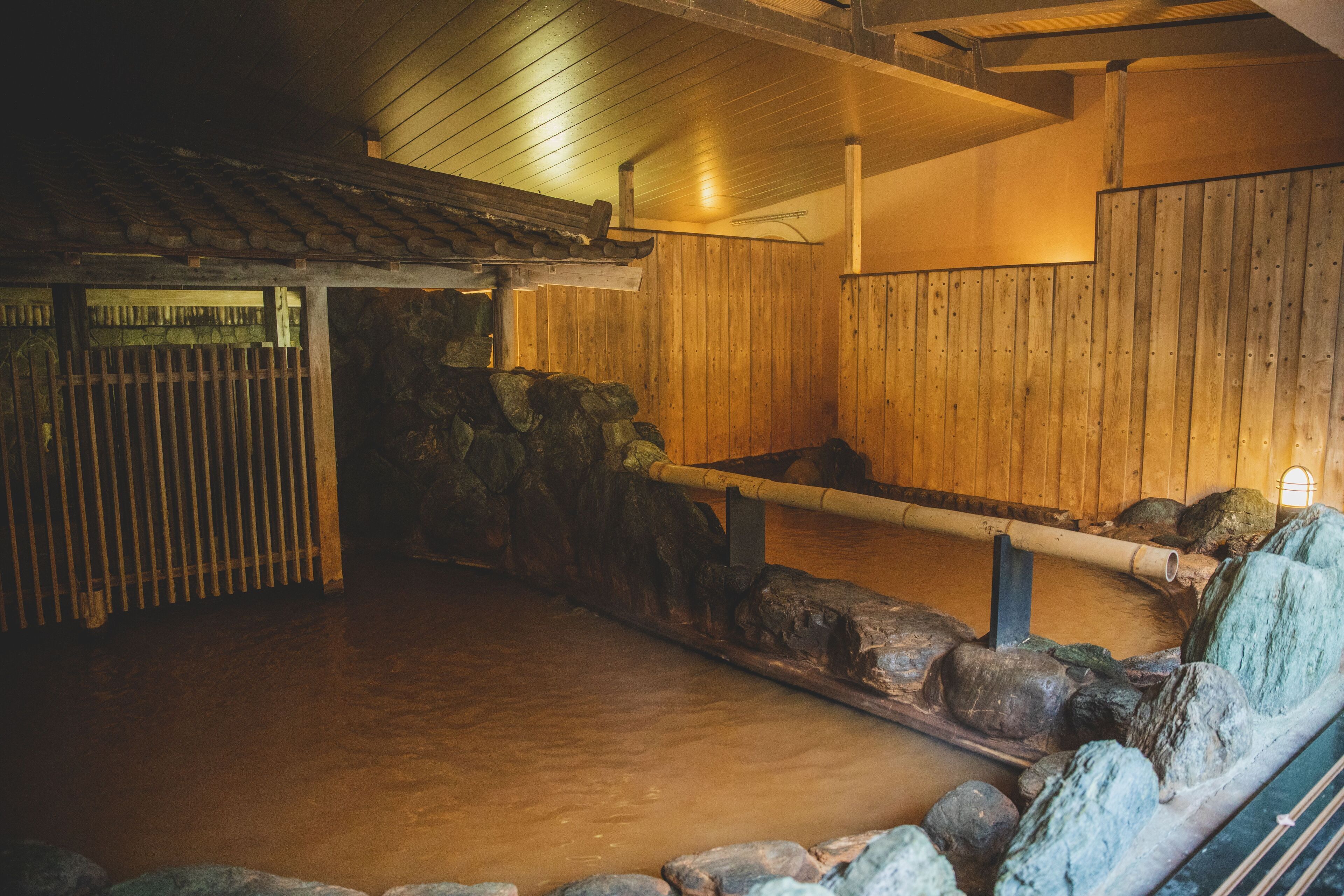 A traditional wooden bathhouse with a stone-lined interior, wooden benches, and a tiled floor.