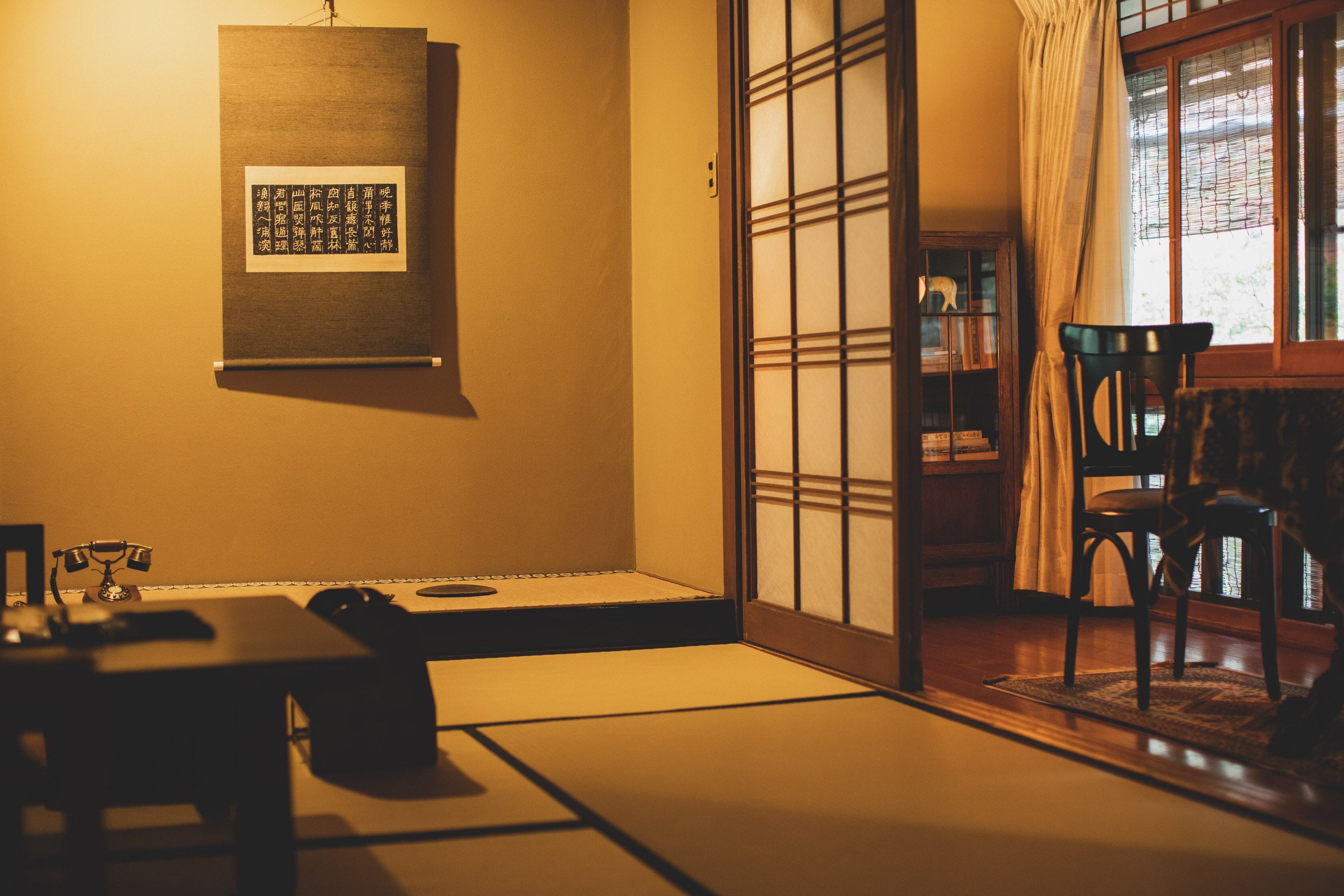A traditional Japanese room with tatami flooring, a sliding door, a black chair, and a small table with a tea set.