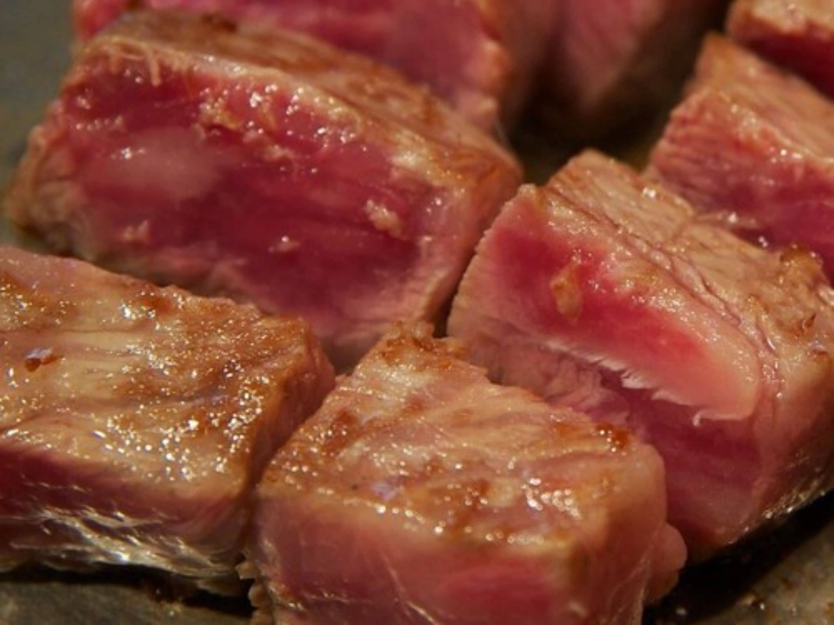 Close-up de carne cozida com centro rosado e exterior dourado.