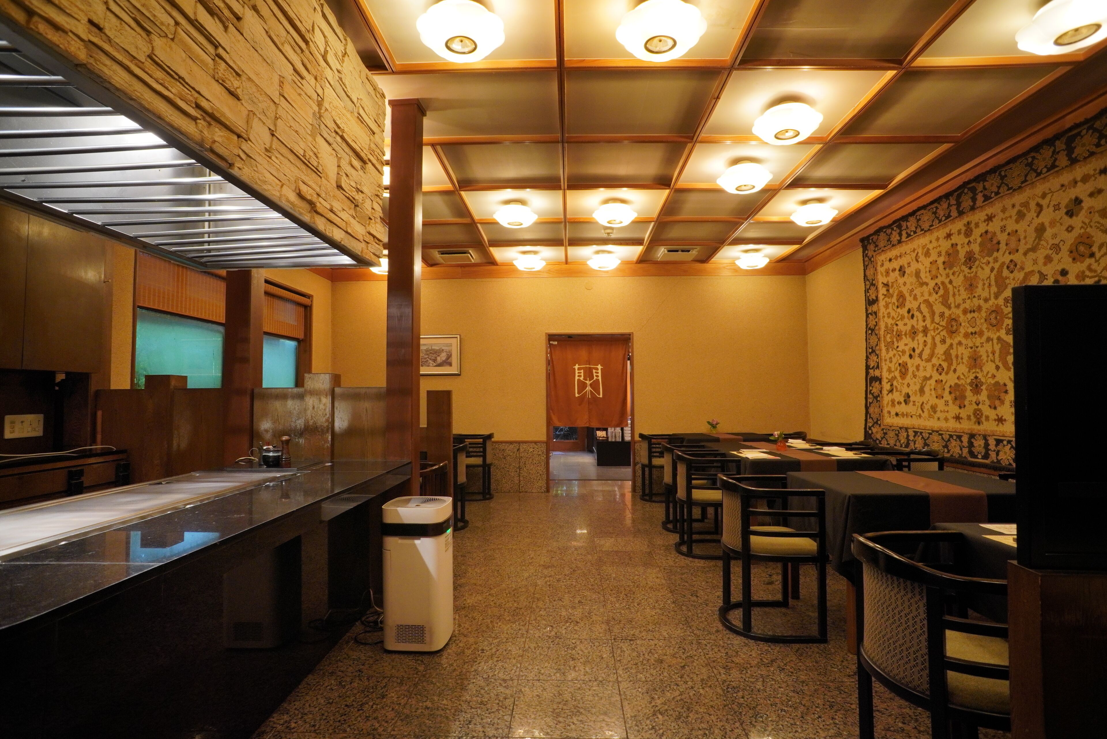 Un restaurante con una barra larga, varias mesas y un muro con diseño.