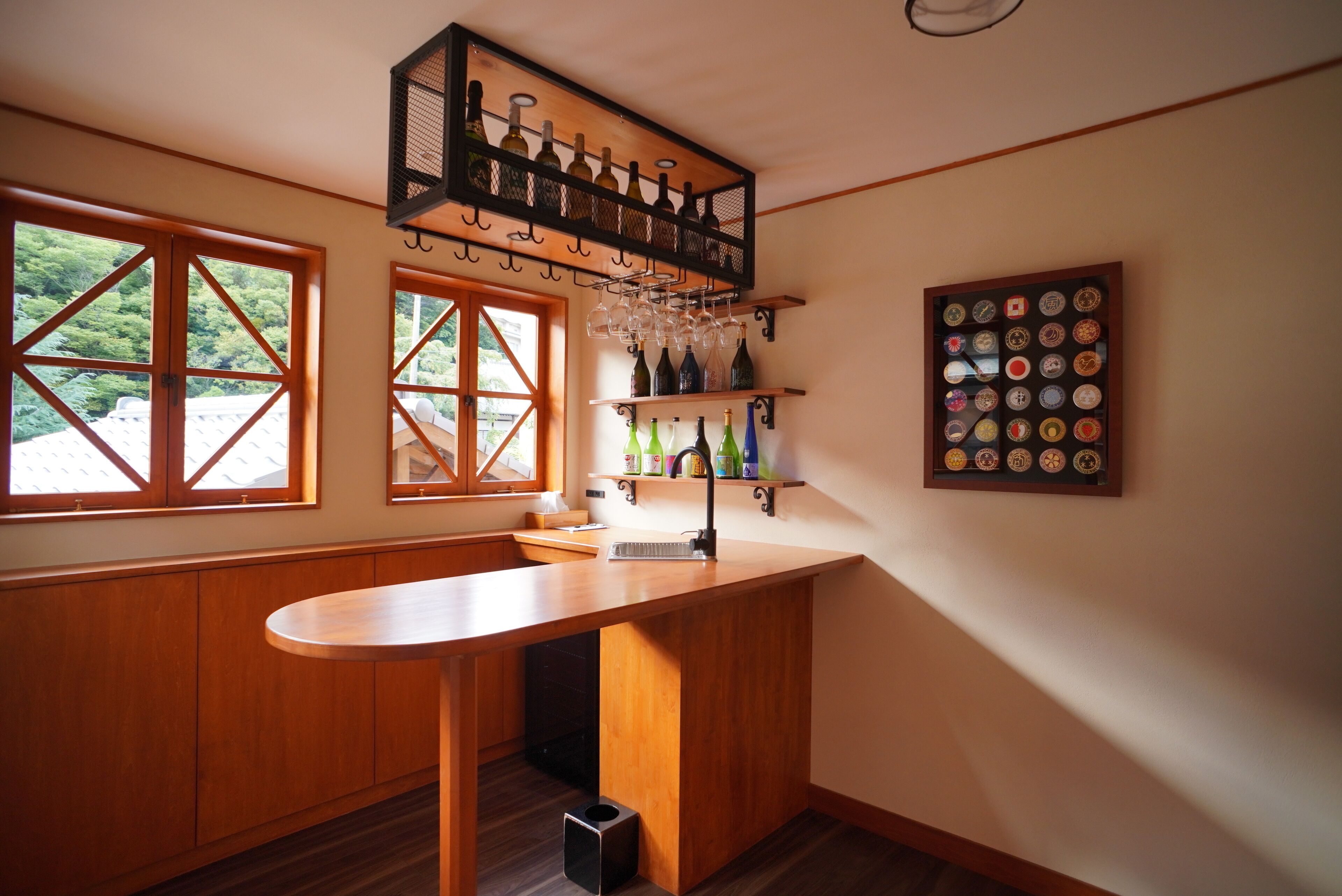 Une cuisine avec des meubles en bois, un coin bar avec des bouteilles de vin et des verres, et un présentoir mural où sont exposées les étiquettes des bouteilles de vin.