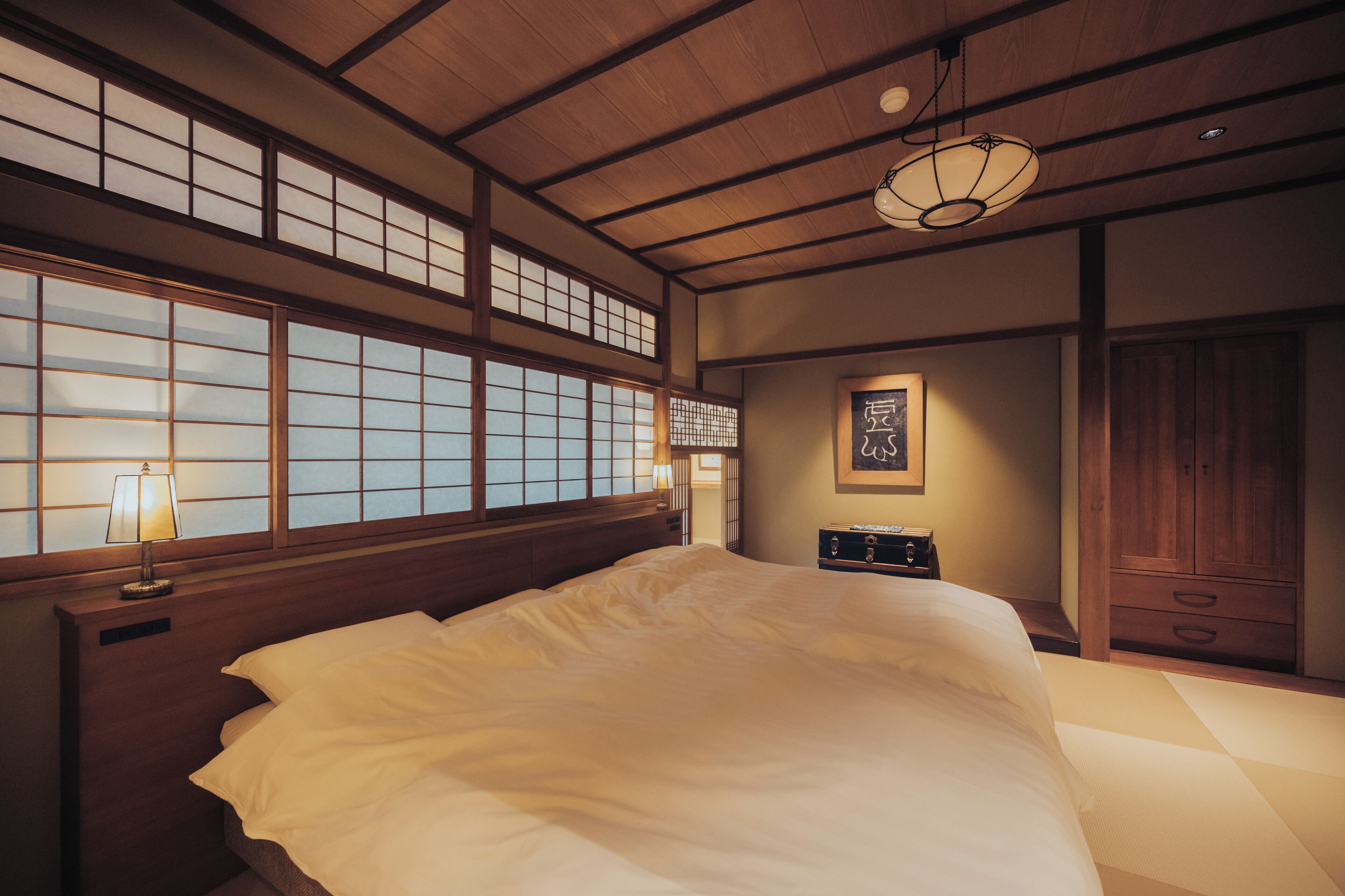 A traditional Japanese-style bedroom with tatami flooring, a large bed, sliding doors, and a ceiling fan.