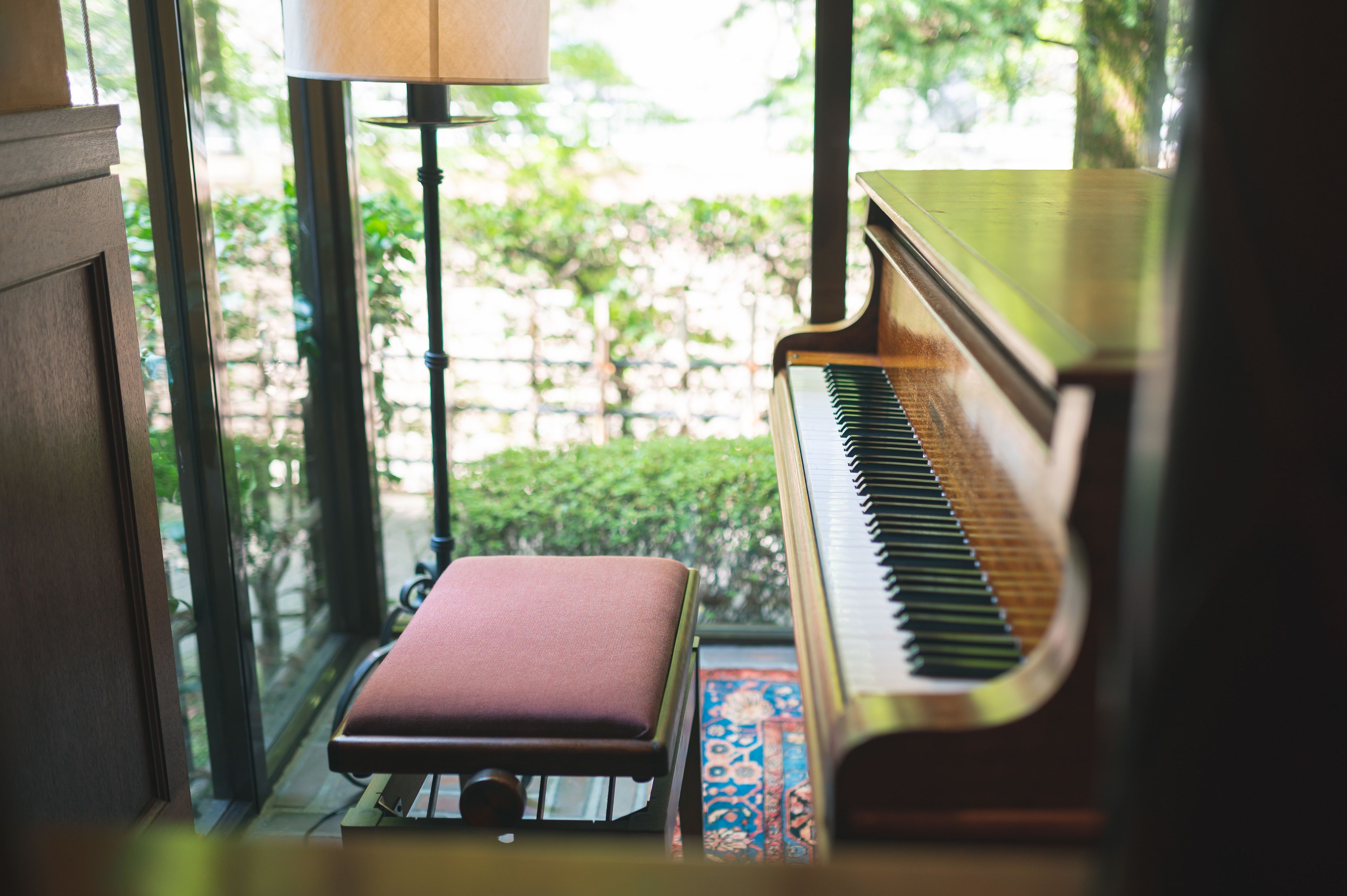 Un piano con un banco en una habitación con ventanas amplias y una lámpara.