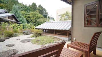 Ein traditioneller japanischer Garten mit einer hölzernen Bank und einem Tisch, umgeben von Steinen und viel Grün.