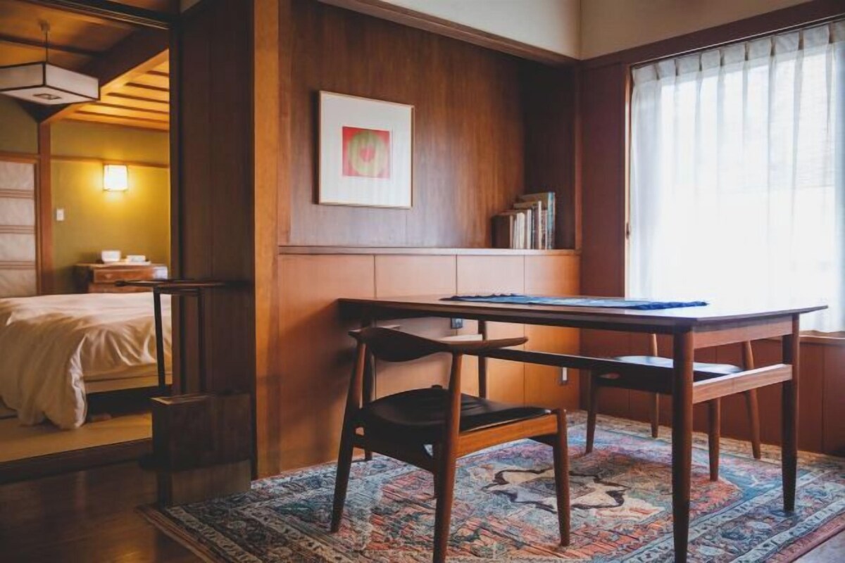 A room with a wooden desk, a chair, a bed, a rug, and a framed picture on the wall.