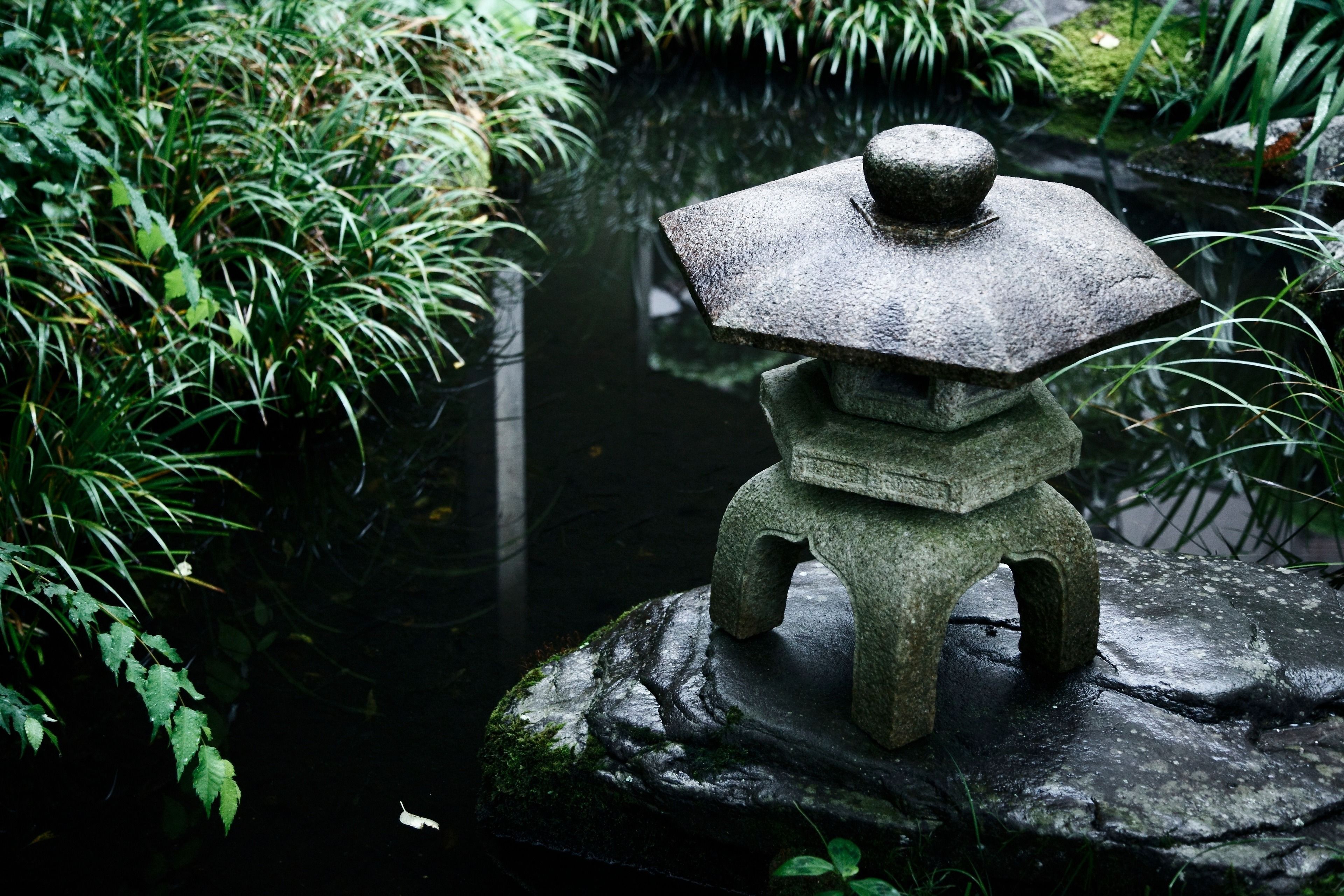 A stone lantern on a rock by a pond surrounded by greenery.