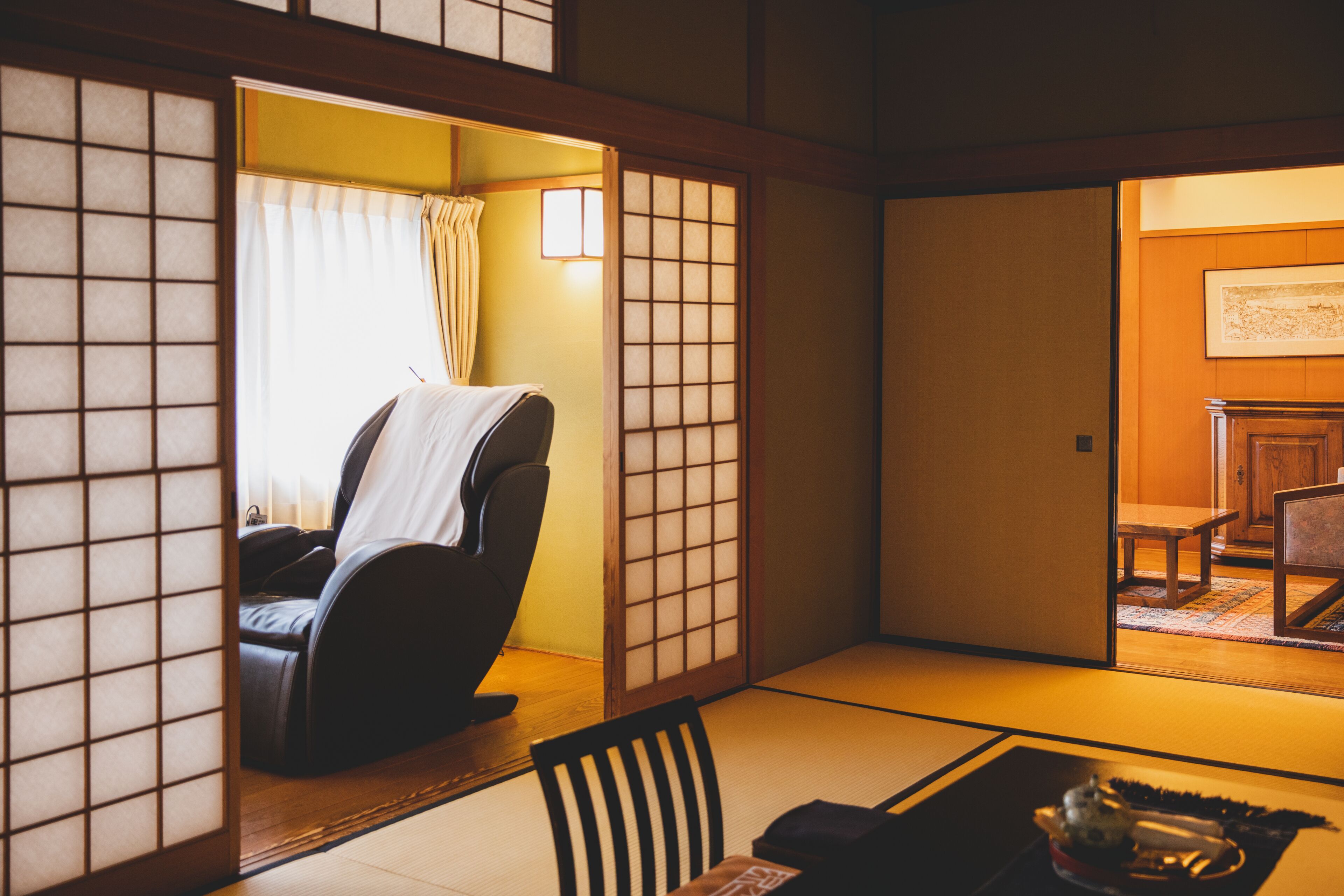 A traditional Japanese room with tatami flooring, a tatami mat table, a low wooden table, a black chair, and a sliding door with a window.