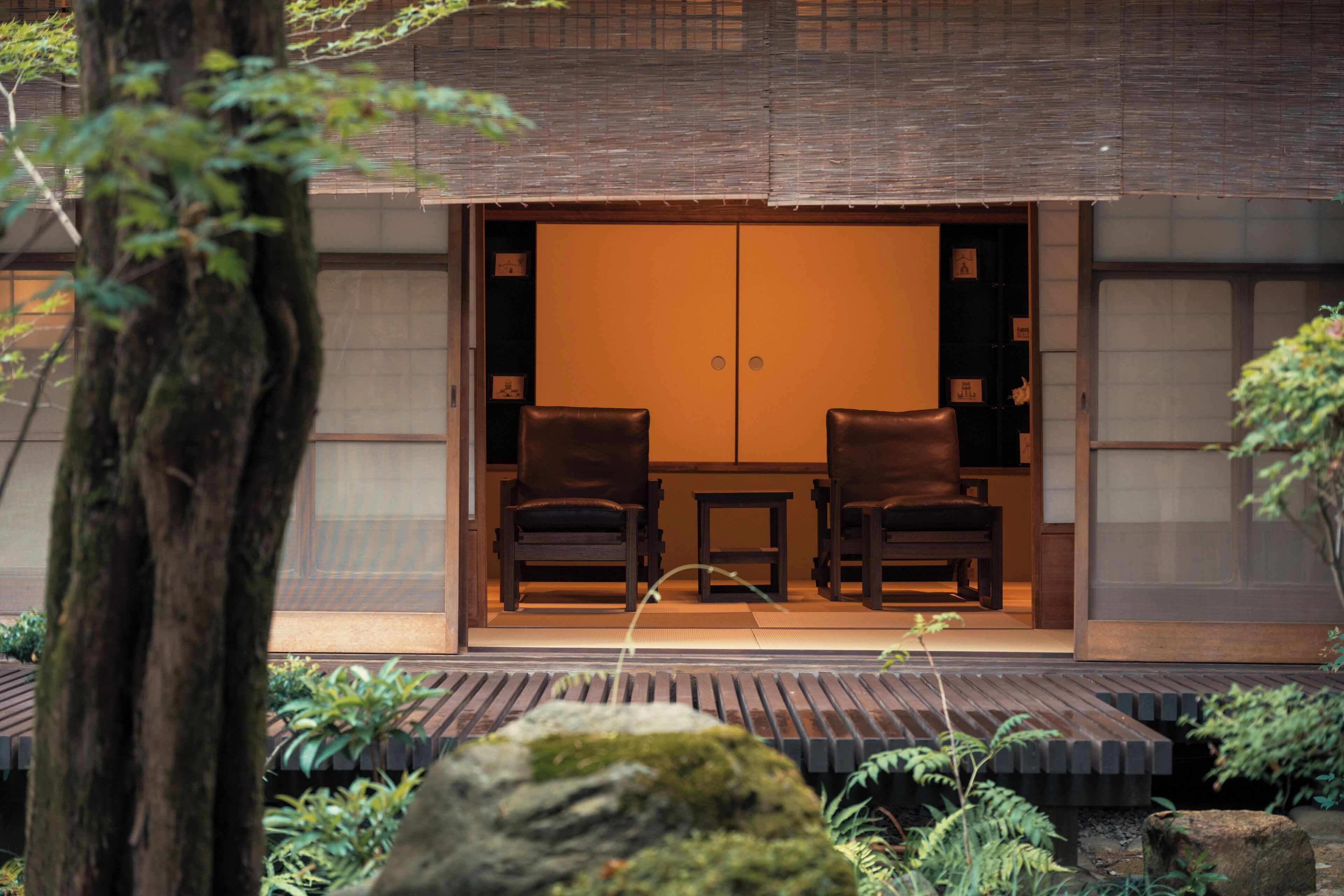 A traditional Japanese room with tatami flooring, two dark wooden chairs, and a sliding door.