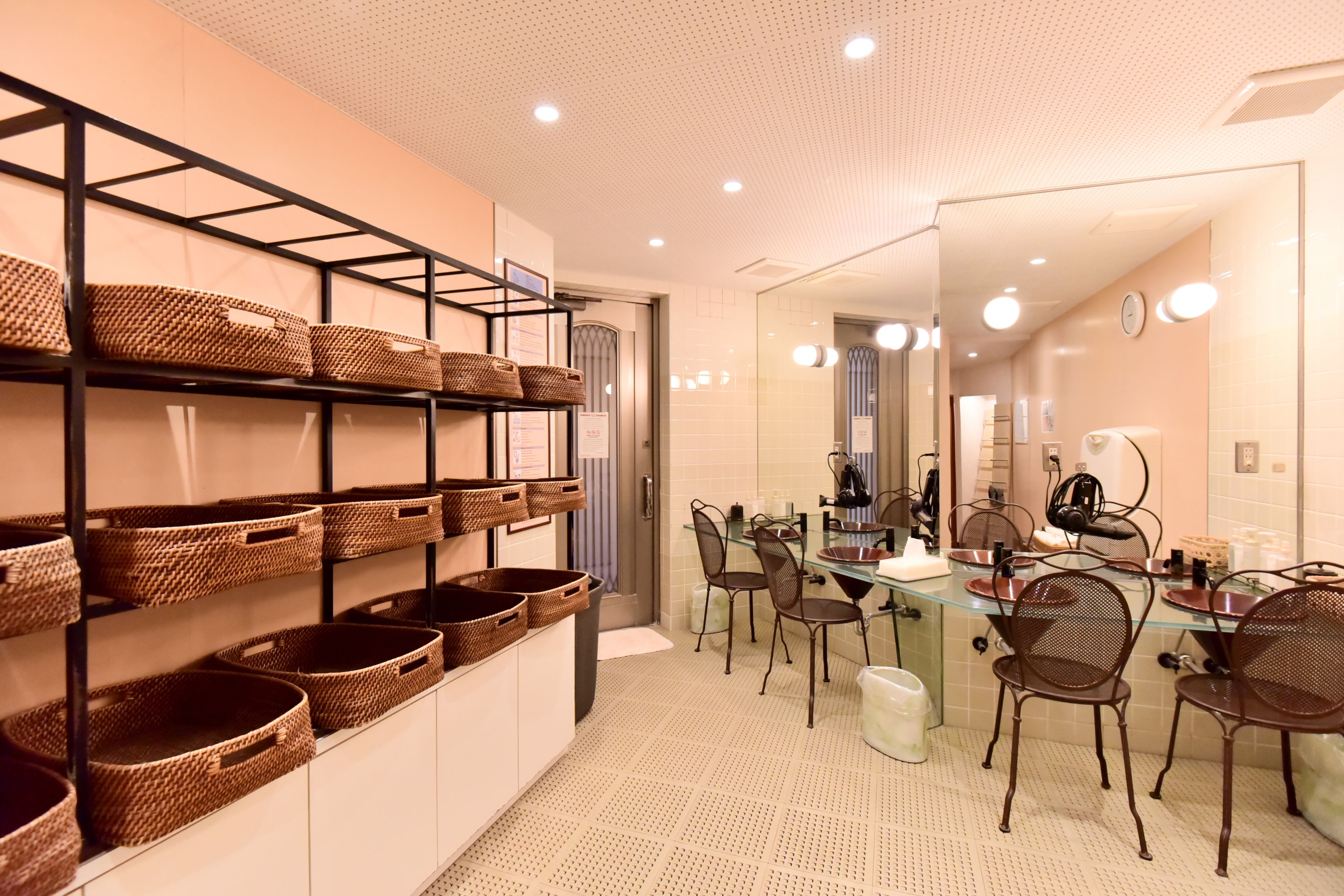 A modern bathroom with a large mirror, wicker baskets on shelves, and a glass table with chairs.