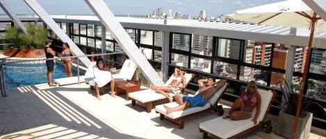 A rooftop pool area with sun loungers and a view of the city skyline.