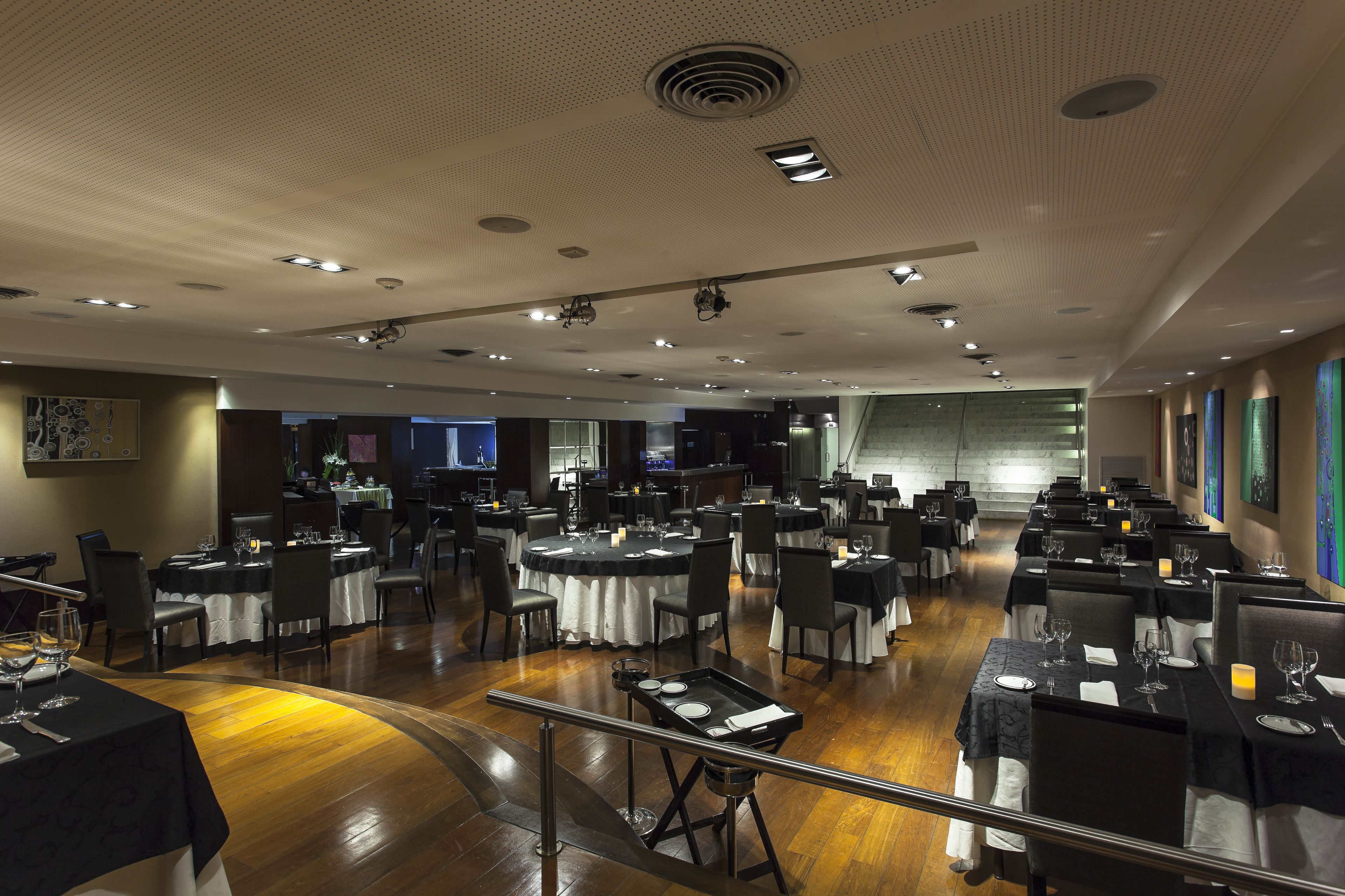 A spacious dining area with multiple tables set for guests, featuring a polished wooden floor and a high ceiling with recessed lighting.