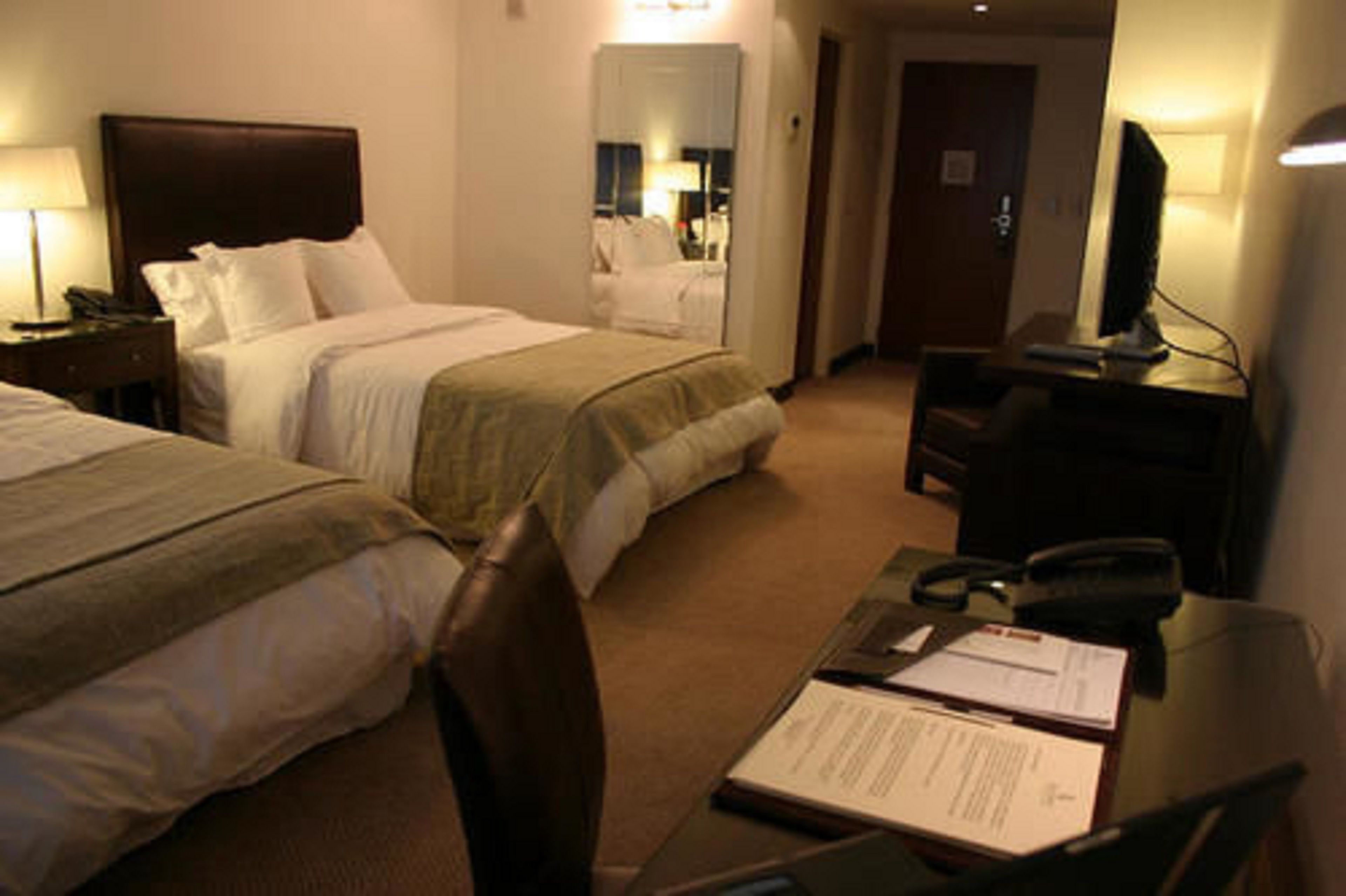 Une chambre d’hôtel avec deux lits, un bureau avec une chaise, une télévision et un miroir.