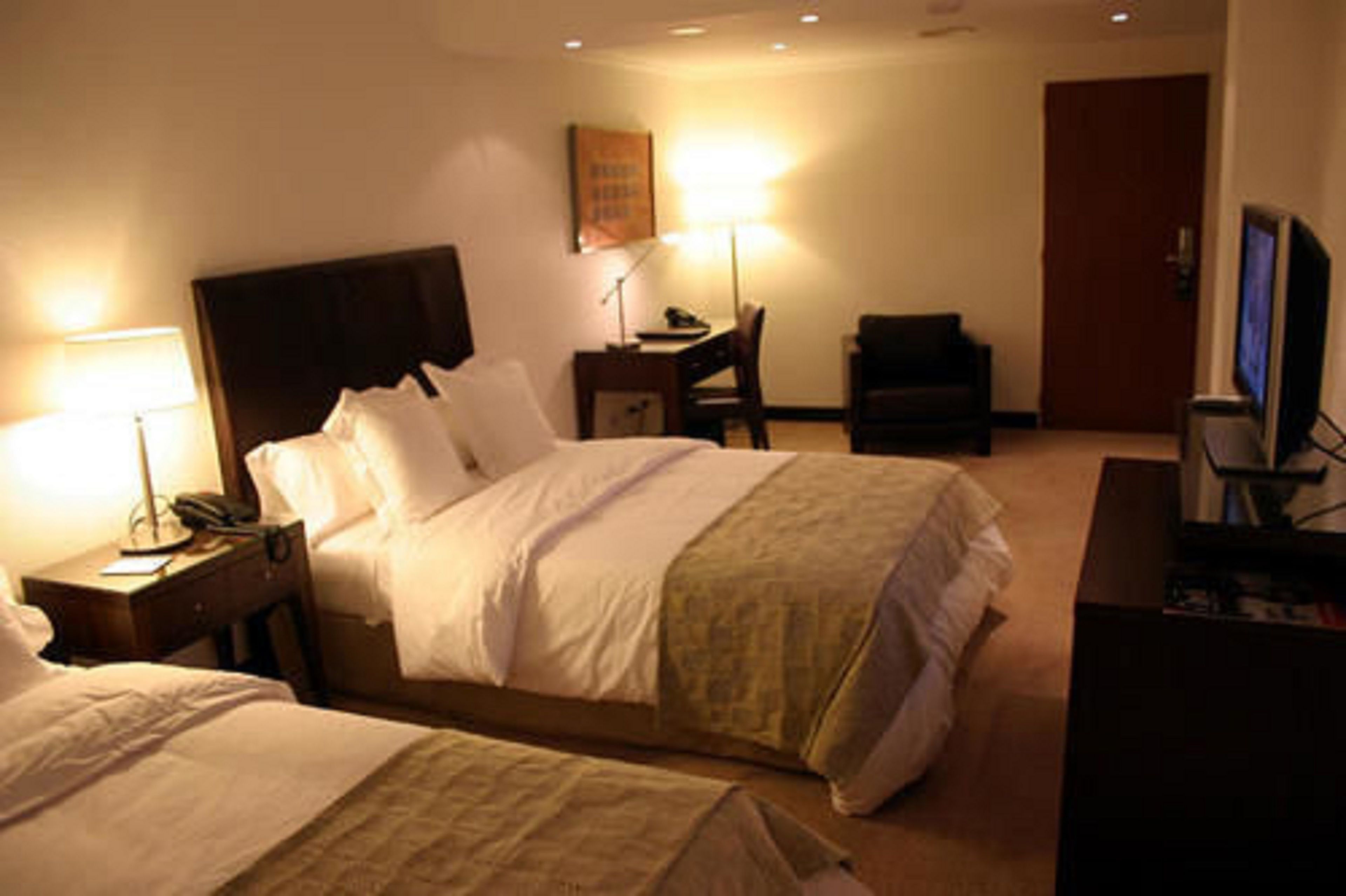 Habitación de hotel con dos camas, un escritorio, una silla, un televisor y una lámpara.