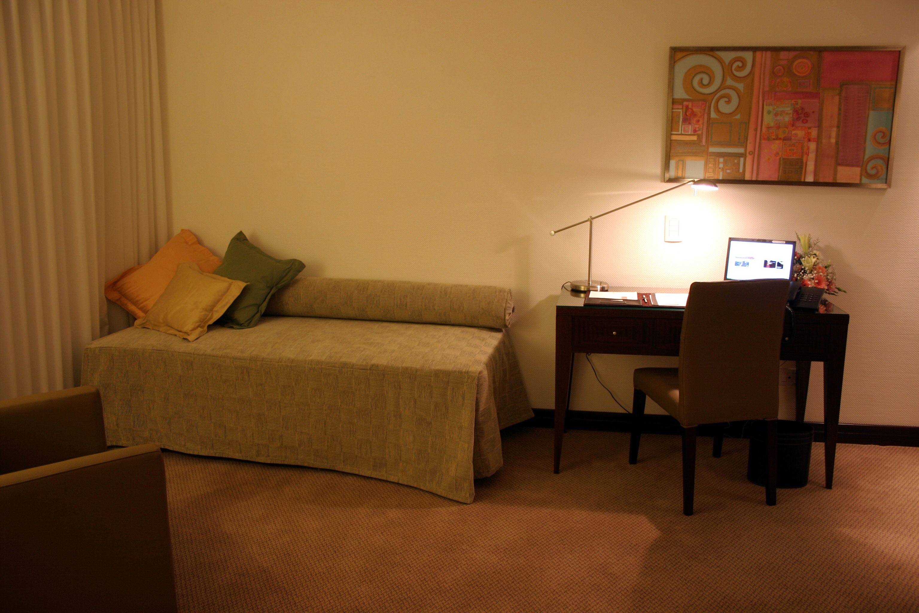 A hotel room with a bed, a desk, a chair, and a computer.