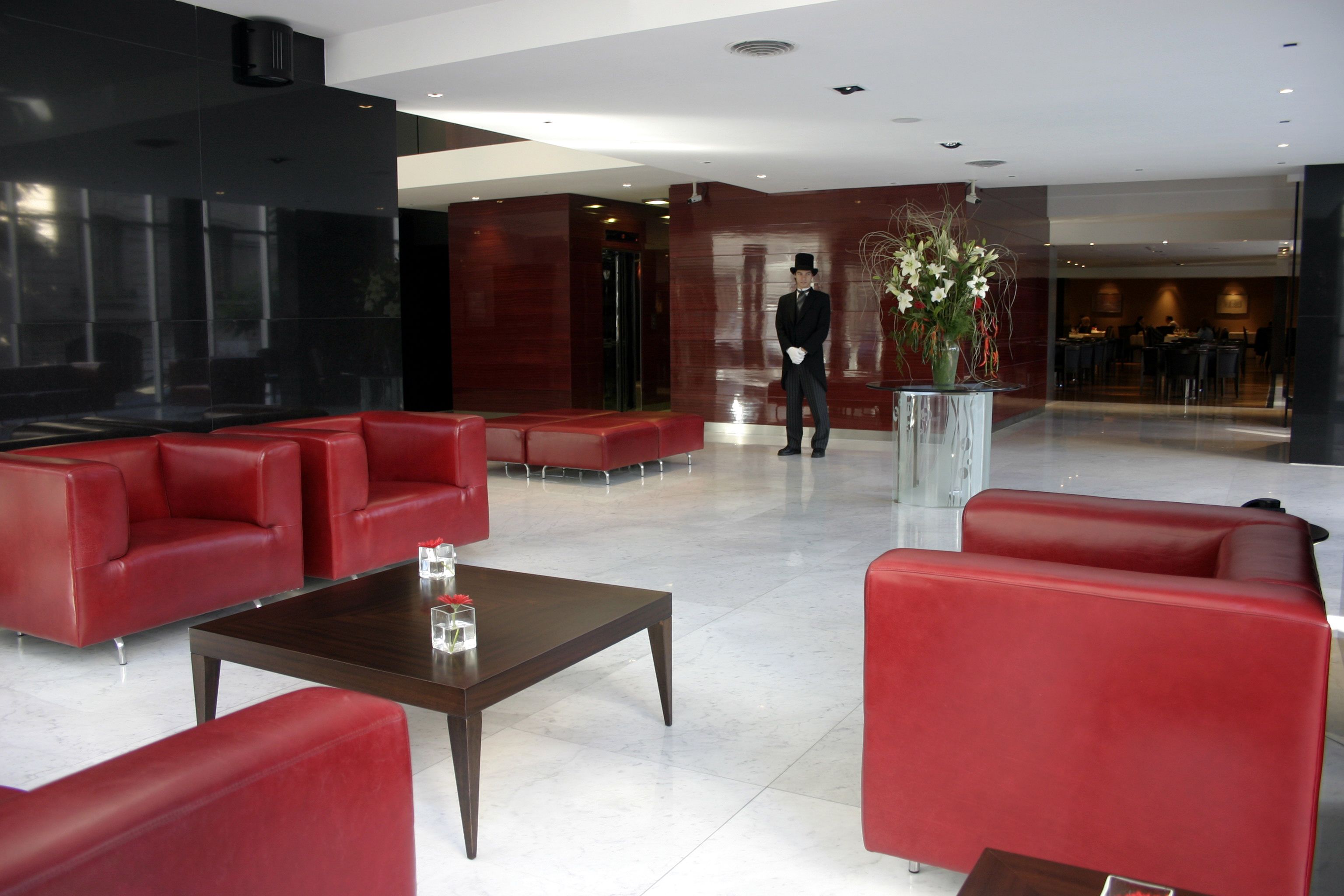 Un hall con sofás de cuero rojo, una mesa de centro y un hombre de pie cerca de un jarrón de flores.