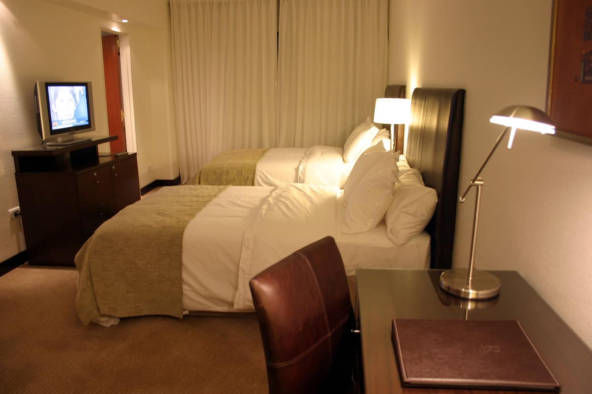 A hotel room with a bed, a desk with a lamp, a TV on a dresser, and a chair.