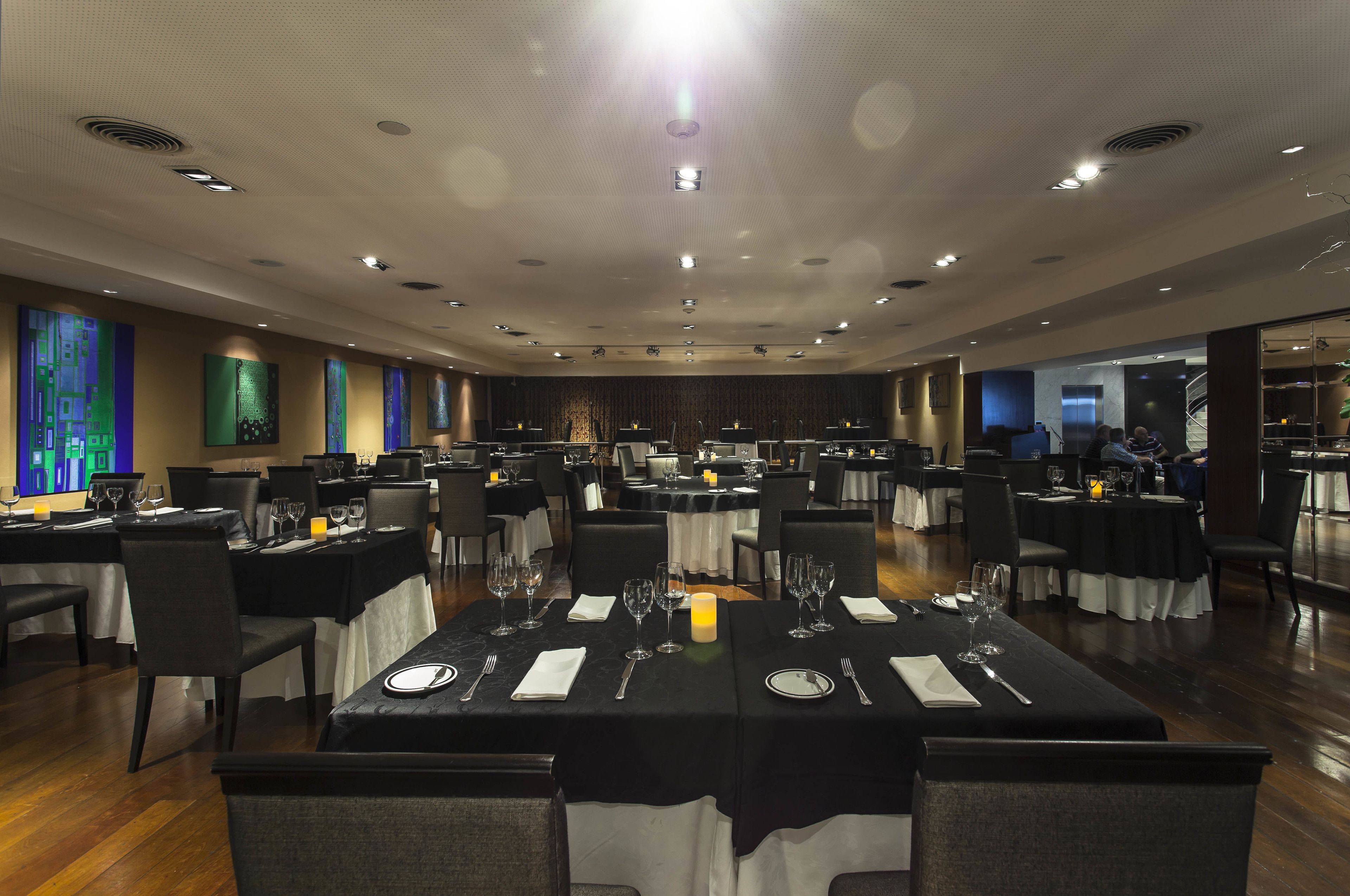 A spacious banquet hall with multiple round tables, each set with white tablecloths, candles, and glassware.