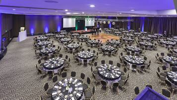 A large conference room with round tables and chairs, a stage, and a screen.