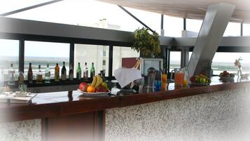Zona de bar con vista a la ciudad, variedad de botellas y frutas frescas en la barra.