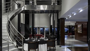 Un vestíbulo moderno de hotel con piso de mármol, una escalera y un área de comedor con mesas y sillas.