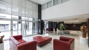 Un vestíbulo amplio con ventanas grandes, asientos rojos y un mostrador de recepción.