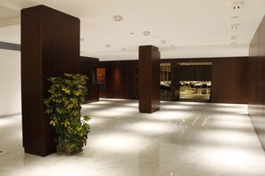 Um hall amplo com piso de mármore, grandes pilares de madeira e uma planta em vaso.