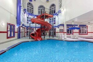 Una piscina interior con un tobogán de agua rojo y una zona de estar con mesas y sillas.