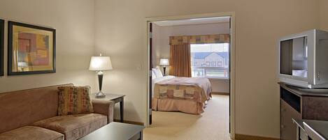 A hotel room with a sofa, a table, a bed, a television, and a window with a view of a building.