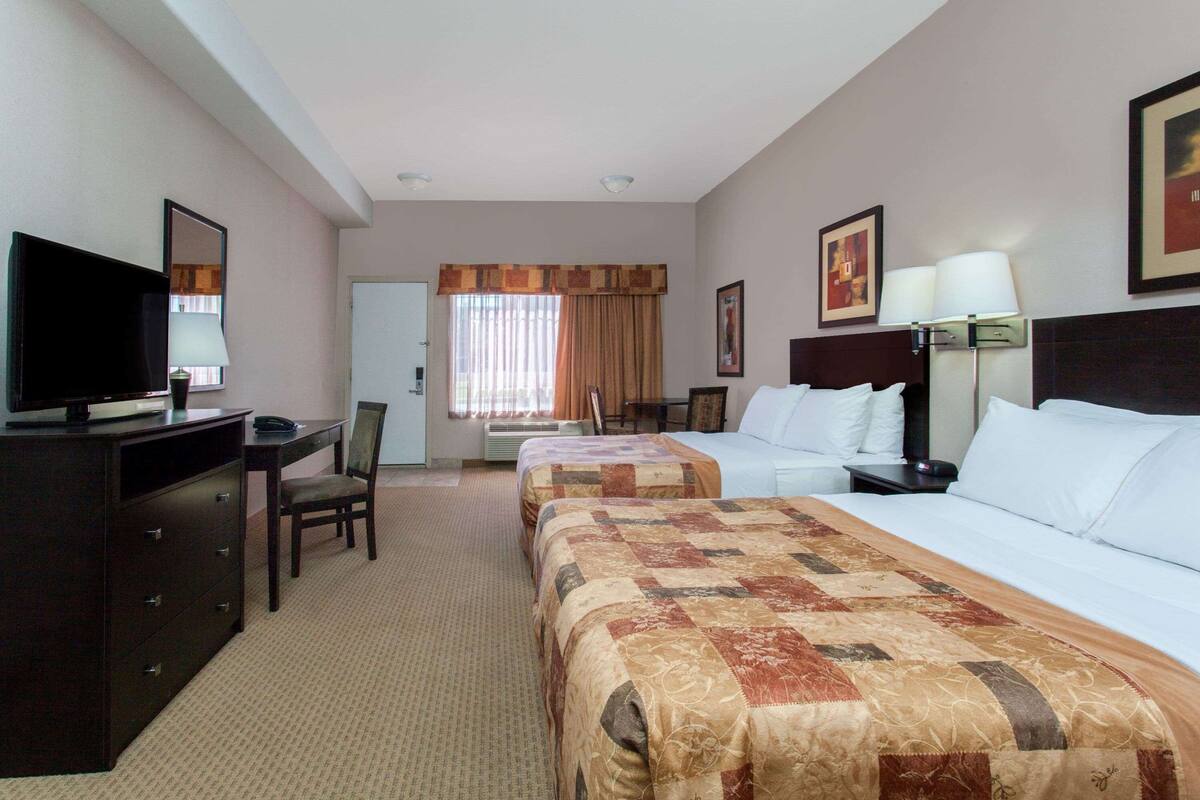 Una habitación de hotel con dos camas, un escritorio, una silla, un televisor y una lámpara.