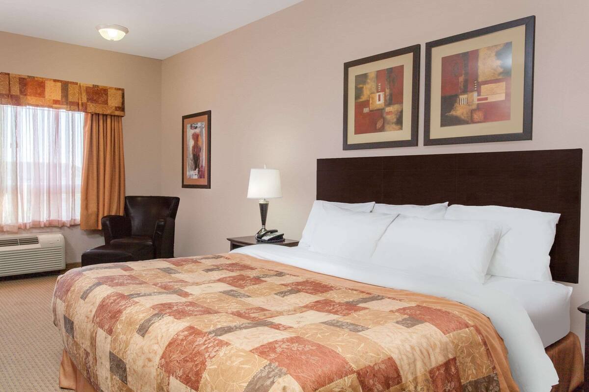 Habitación de hotel con una cama grande, una silla, una lámpara y dos cuadros en la pared.