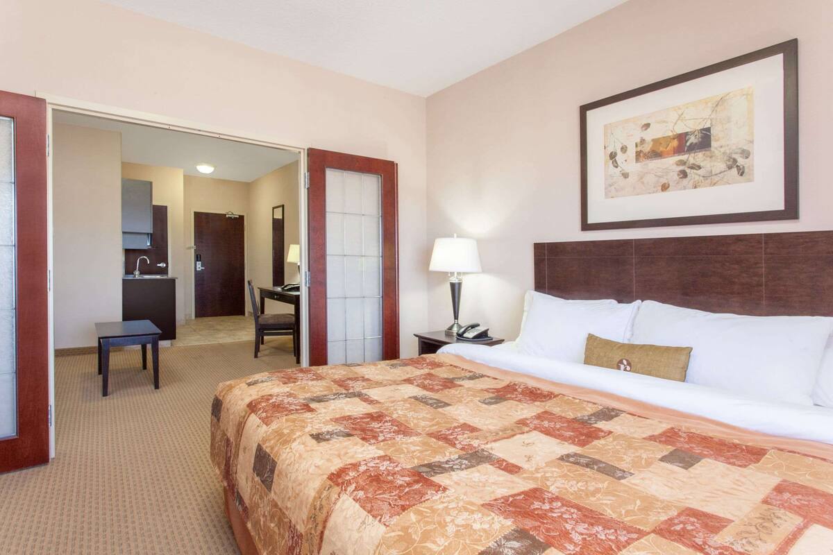 Habitación de hotel con una cama grande, un escritorio, una silla y un baño visible a través de una puerta abierta.