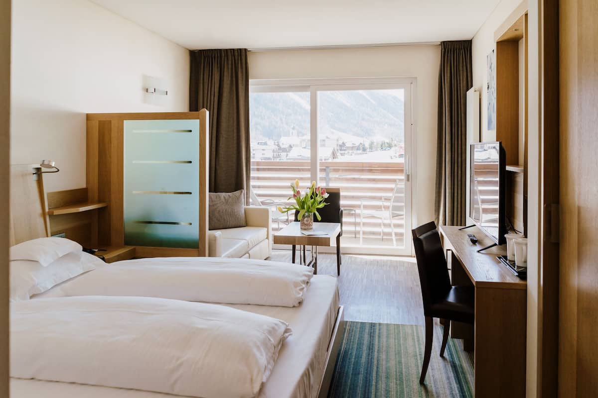 Habitación de hotel con dos camas, un escritorio, una silla, televisión y vistas a las montañas.