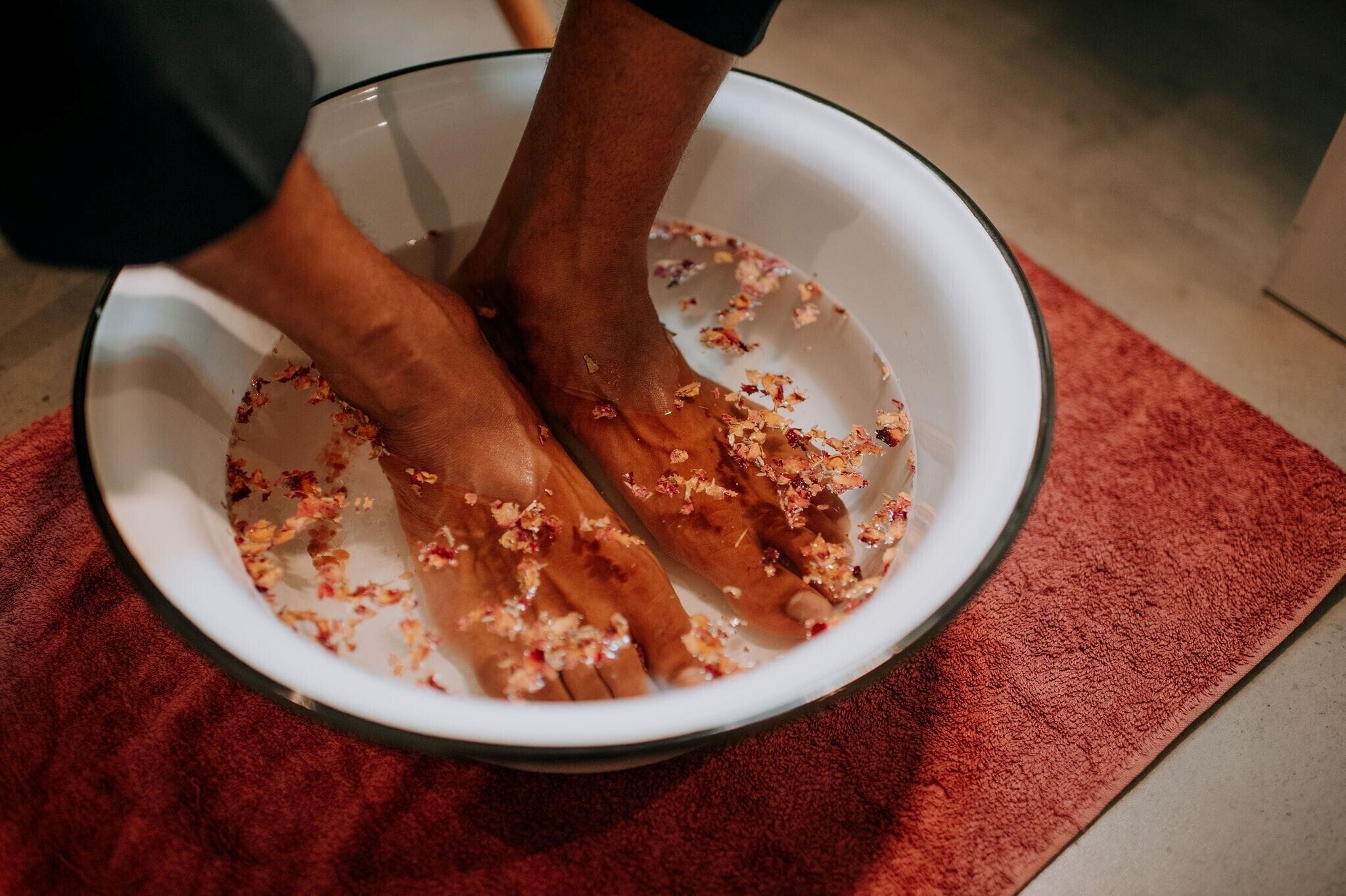 Pies en un recipiente con agua y pétalos de flores.