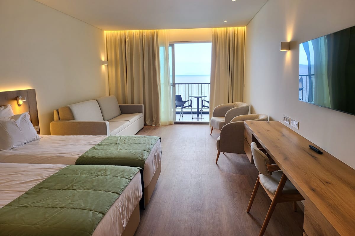 A hotel room with two beds, a sofa, a wooden desk, and a TV.
