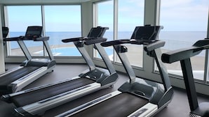 A gym with treadmills and large windows overlooking a body of water. - Rocamar Lido Resort (Santa Cruz)