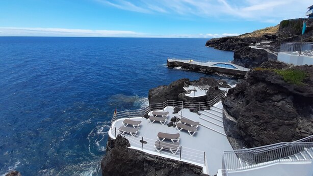 A coastal cliffside with a pool area featuring sun loungers and a staircase leading down to the water. - Rocamar Lido Resort (Santa Cruz)