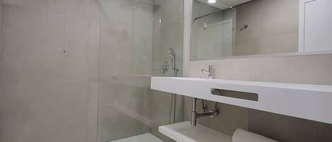 A modern bathroom with a glass-enclosed shower, a white sink with a mirror above, and a towel rack.