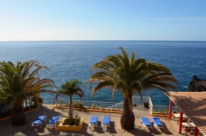 A terrace with sun loungers, palm trees, and a view of the sea.