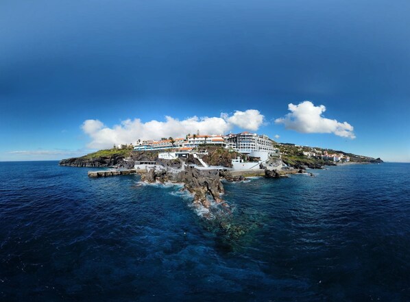 A coastal hotel with multiple buildings, a rocky shoreline, and clear blue skies.