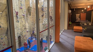 An indoor climbing facility with multiple climbing walls, padded flooring, and a seating area with cushions.