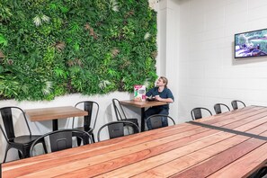 A dining area with a wooden table, chairs, a TV, and a wall with a green plant wall. - Rock Solid Backpackers Rotorua (Rotorua)
