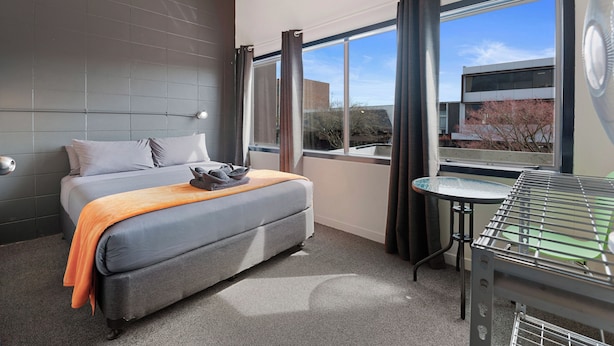 A hotel room with a bed, a small table, a grill, and a view of the outside.