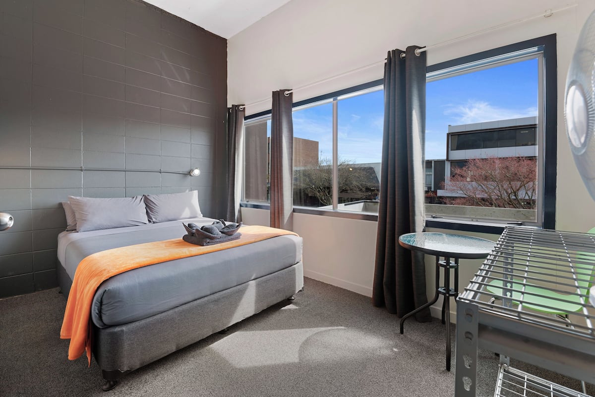 A hotel room with a bed, a small table, a grill, and a view of the outside.