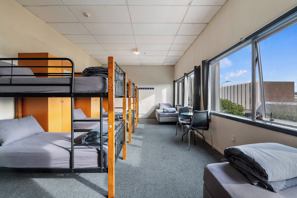 A dormitory room with bunk beds, a desk, and a chair.