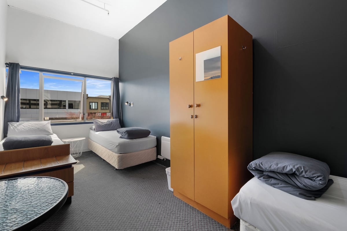 A modern hotel room with a large wardrobe, a sofa bed, a small round table, and a view of the outside through a large window.