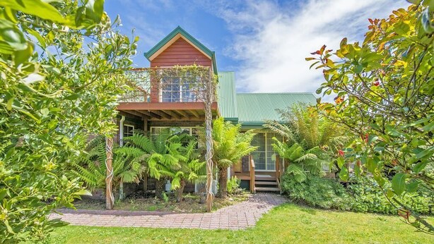 A two-story house with a green roof, surrounded by lush greenery and a brick pathway. - Aloft Boutique Accommodation (Strahan)